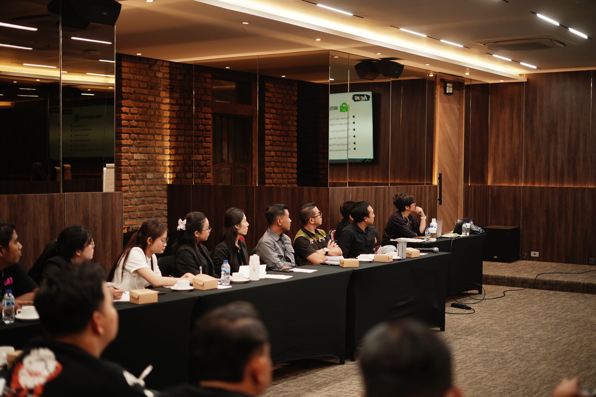 Participants at a long black-draped table watching a presentation in the Omong-Omong meeting room