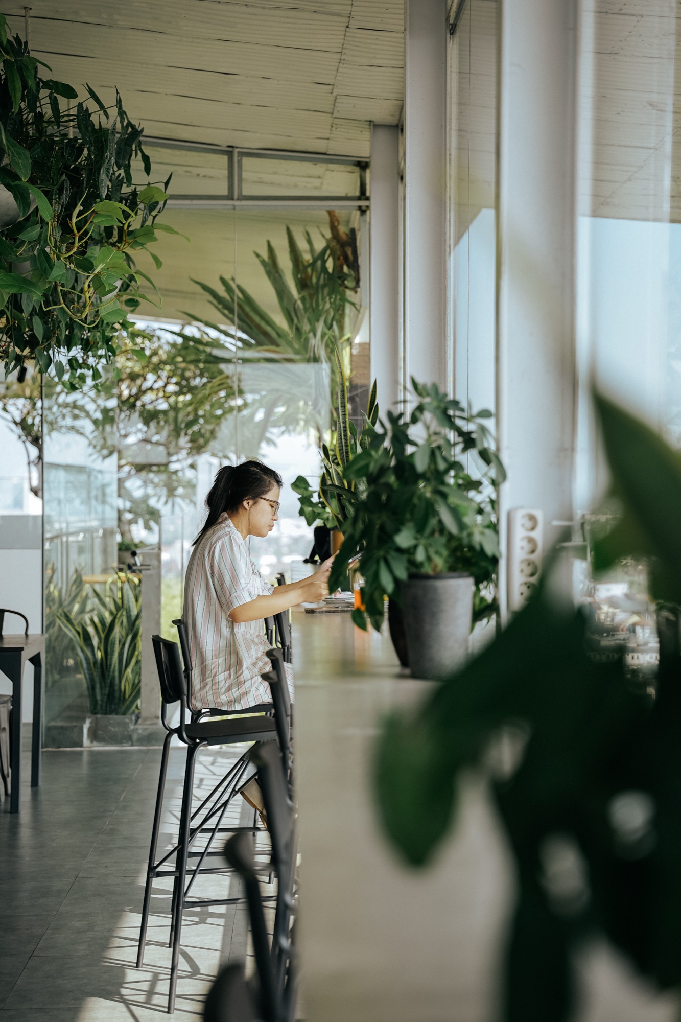 Guest on a bar stool checking her phone among potted plants at Alfresco Dining